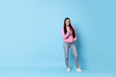 Photo of Smiling woman with smartphone on light blue background. Space for text