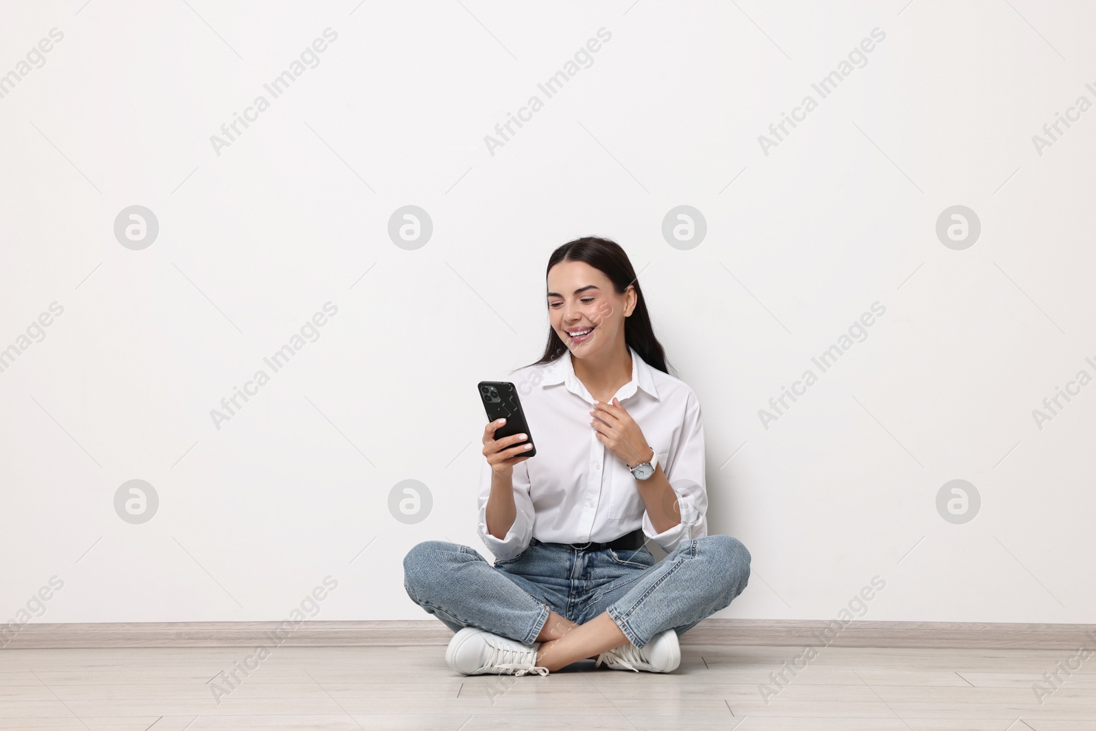 Photo of Smiling woman with smartphone on floor against white background