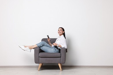 Photo of Smiling woman with smartphone sitting on armchair against white wall