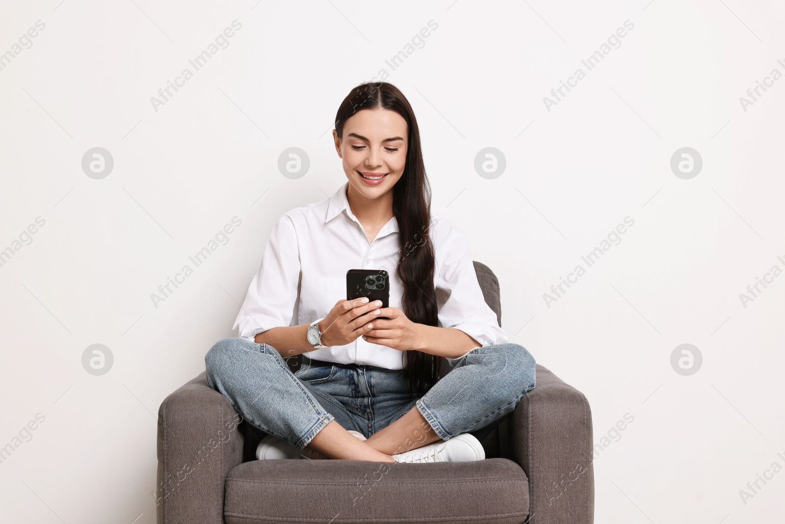 Photo of Smiling woman with smartphone sitting on armchair against white background