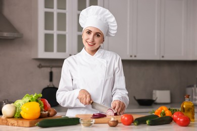 Photo of Professional chef cutting onion at table in kitchen