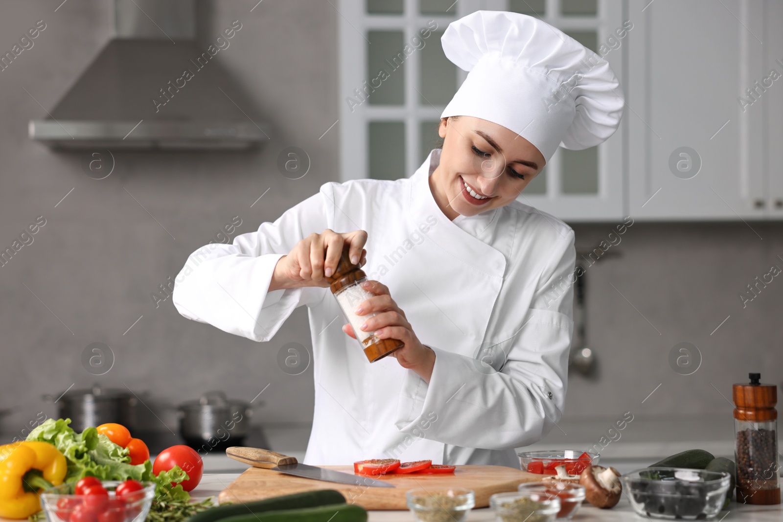 Photo of Professional chef seasoning tomatoes at table in kitchen