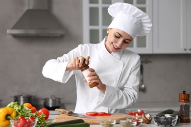 Photo of Professional chef seasoning tomatoes at table in kitchen