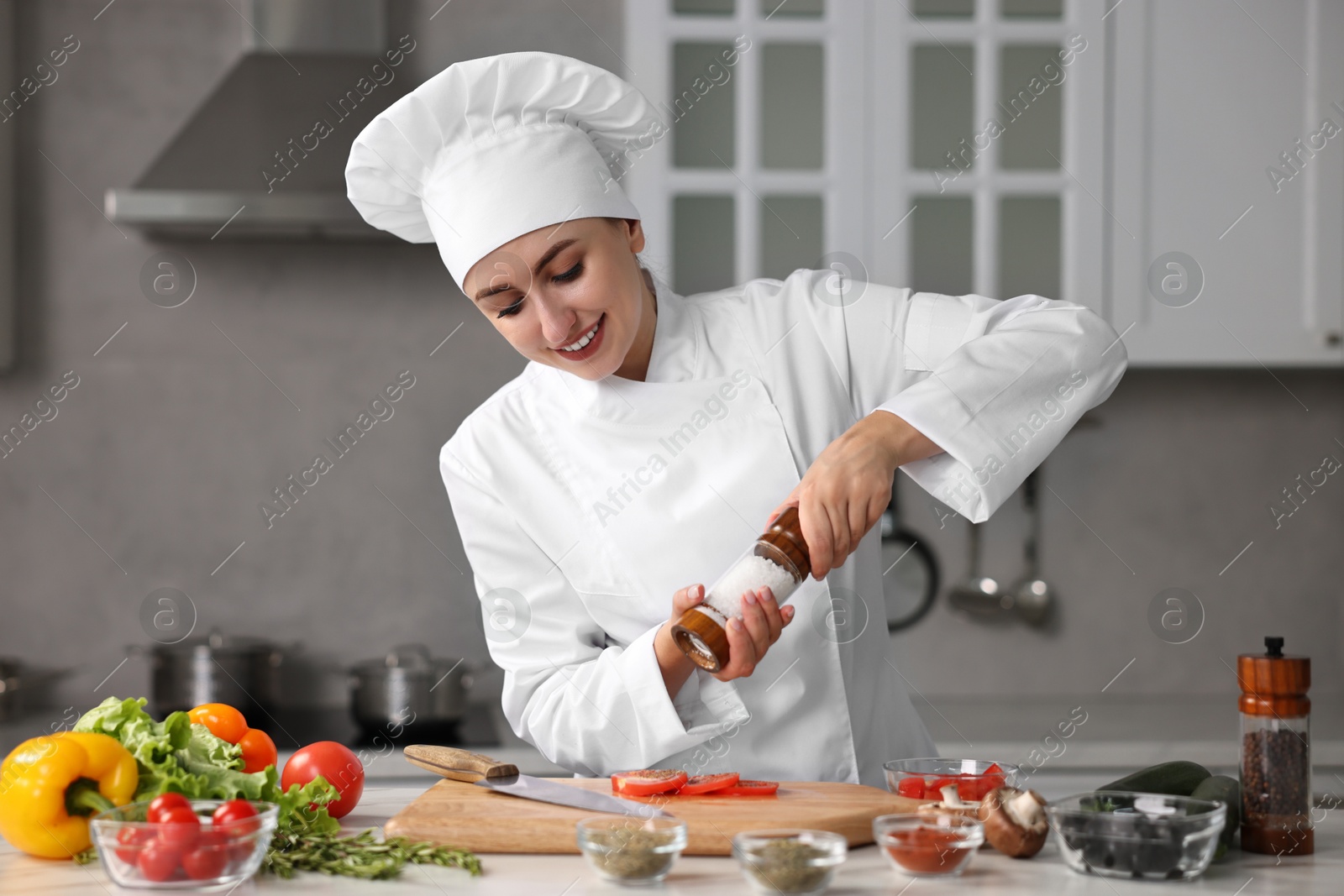 Photo of Professional chef seasoning tomatoes at table in kitchen