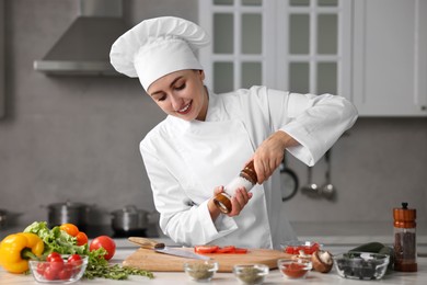 Photo of Professional chef seasoning tomatoes at table in kitchen