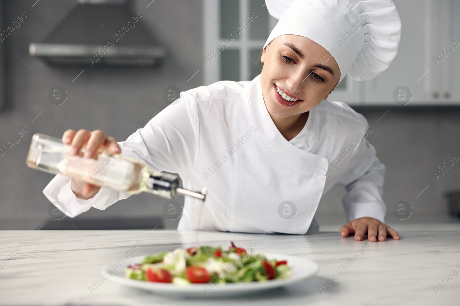 Photo of Professional chef pouring oil onto delicious salad at white marble table in kitchen