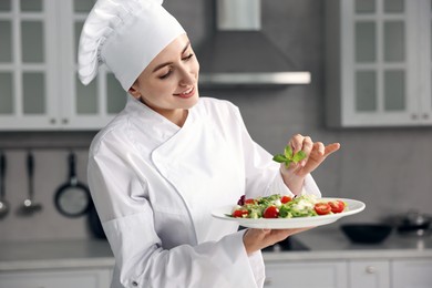 Professional chef decorating delicious salad with basil in kitchen