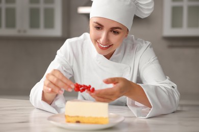 Photo of Professional chef decorating delicious cheesecake with red currants at white marble table in kitchen