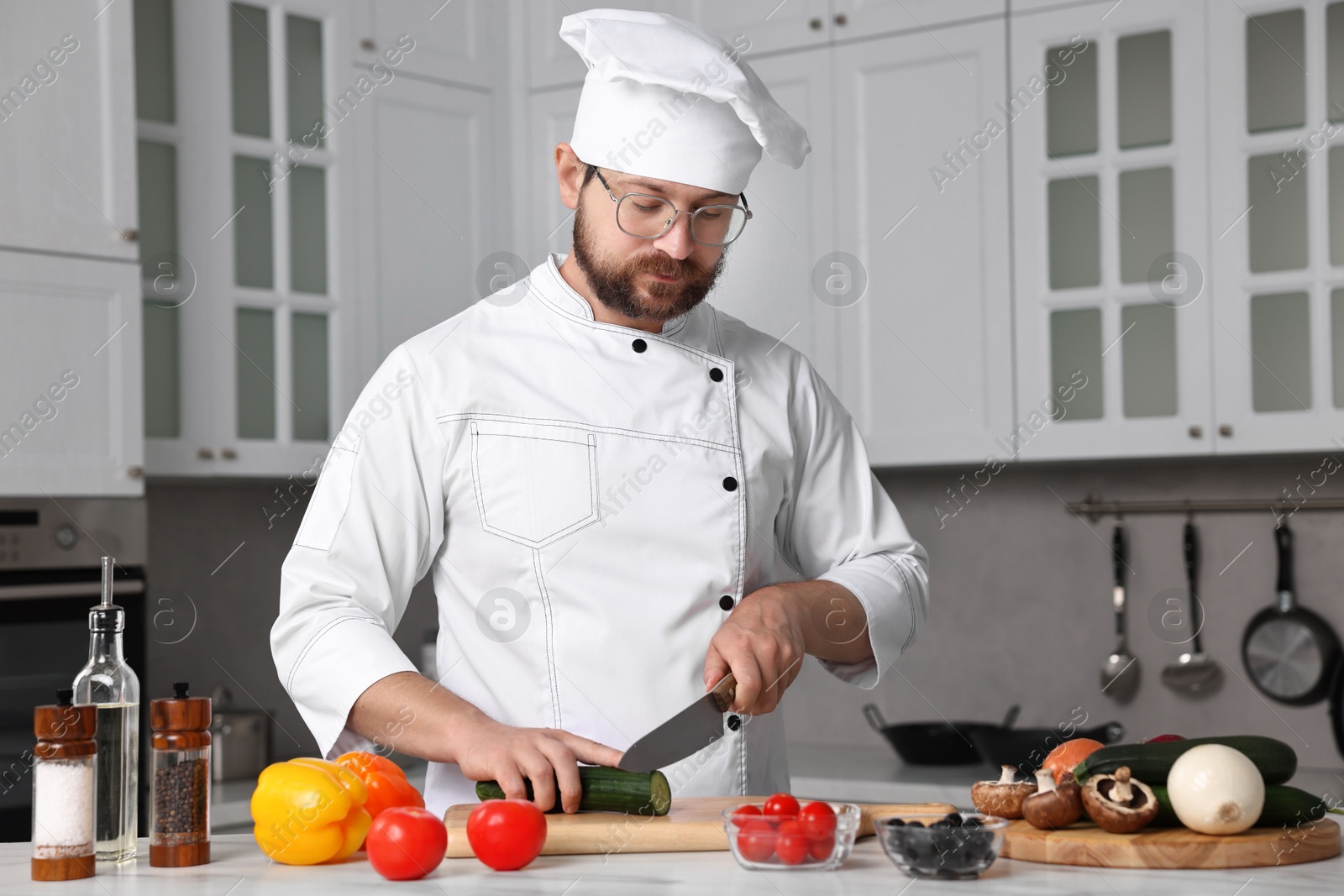 Photo of Professional chef cutting cucumber at white marble table in kitchen