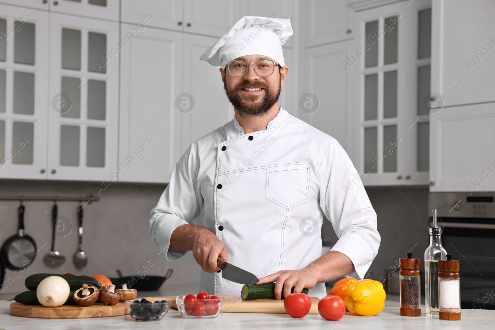 Photo of Professional chef cutting cucumber at white marble table in kitchen