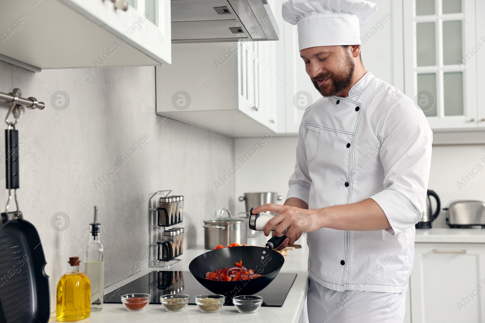 Photo of Professional chef adding salt into frying pan in kitchen