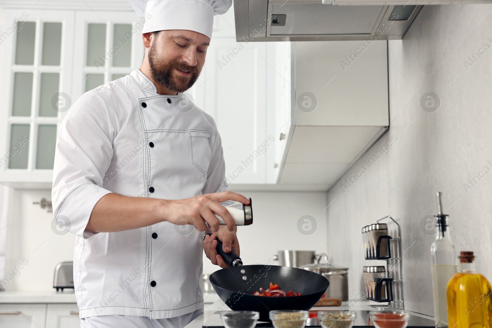 Photo of Professional chef adding salt into frying pan in kitchen