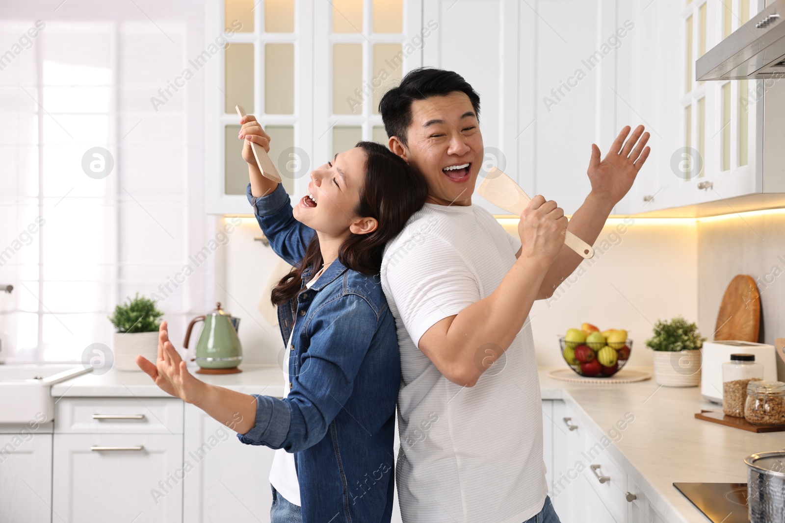 Photo of Happy lovely couple singing together while cooking in kitchen