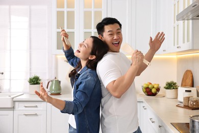 Photo of Happy lovely couple singing together while cooking in kitchen