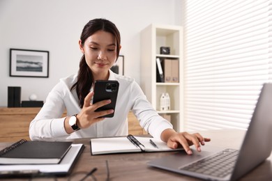 Beautiful businesswoman with smartphone at table in office