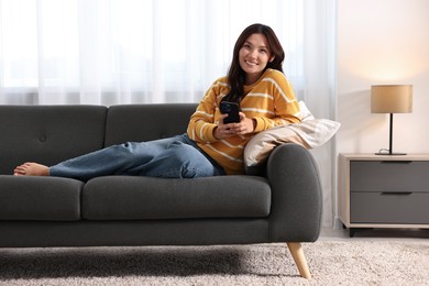 Photo of Smiling woman with smartphone on sofa at home