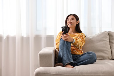 Photo of Smiling woman with smartphone on sofa at home. Space for text