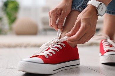 Photo of Woman tying shoelace of red sneaker indoors, closeup