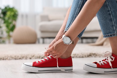 Photo of Woman tying shoelace of red sneaker indoors, closeup