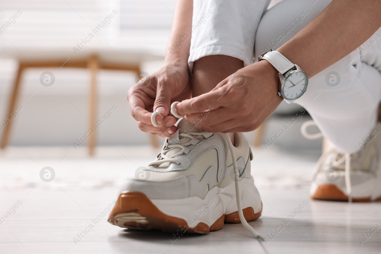 Photo of Woman tying shoelace of sneaker indoors, closeup. Space for text