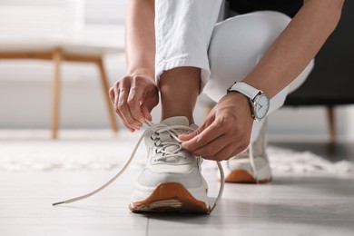 Photo of Woman tying shoelace of sneaker indoors, closeup