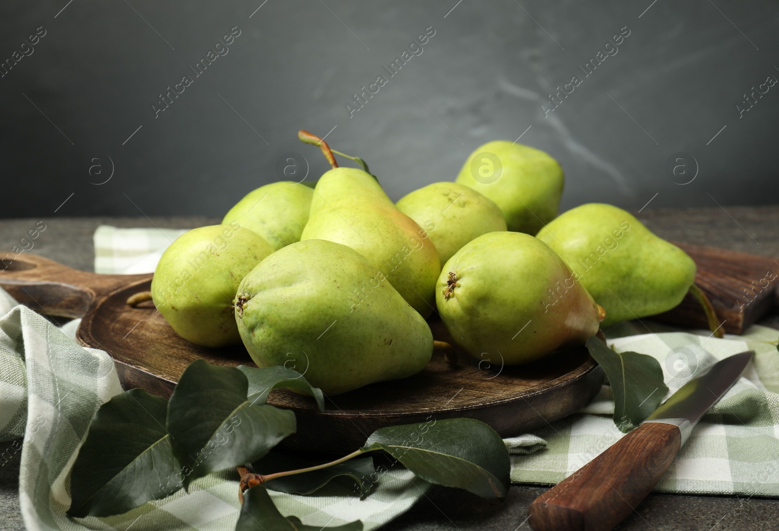 Photo of Many fresh ripe pears, green leaves and knife on grey table