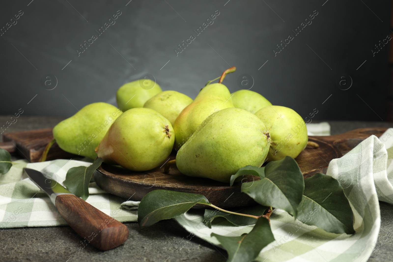 Photo of Many fresh ripe pears, green leaves and knife on grey table