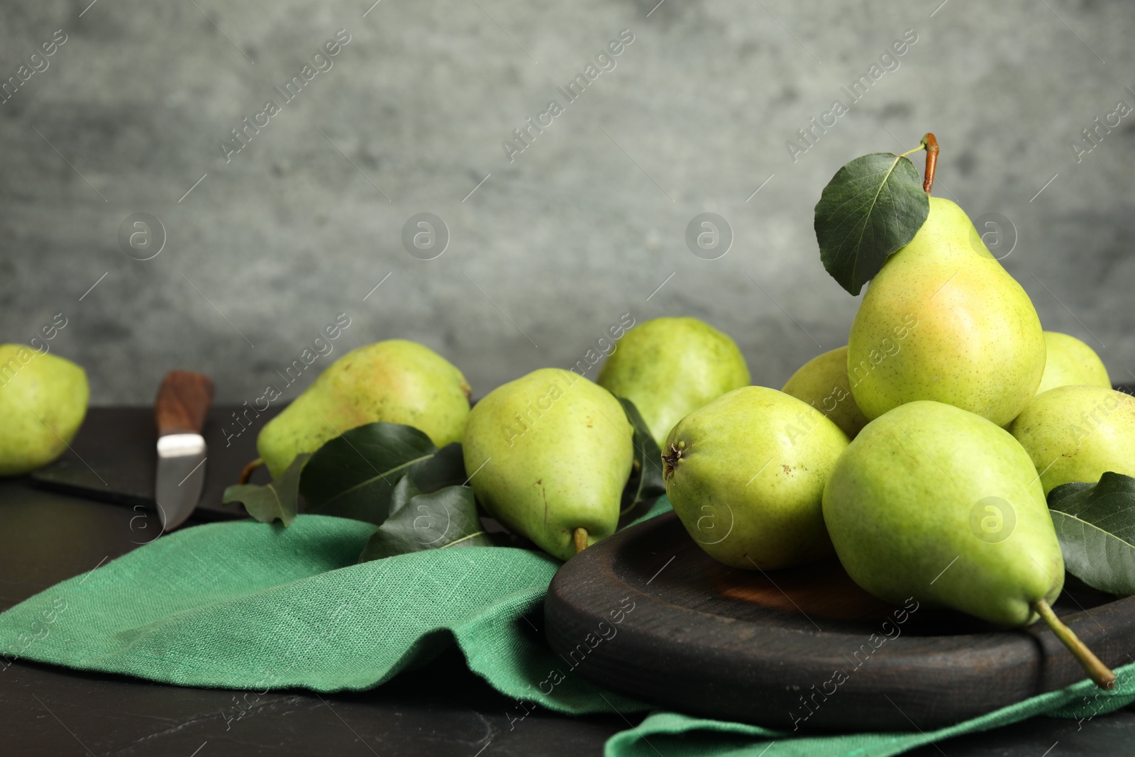 Photo of Many fresh ripe pears and green leaves on black table