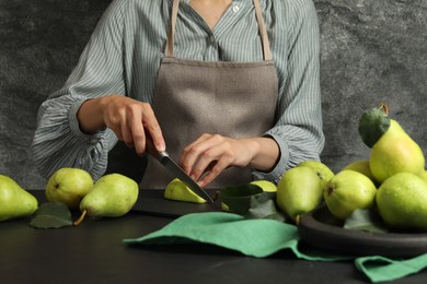 Photo of Woman cutting fresh ripe pear at black table, closeup