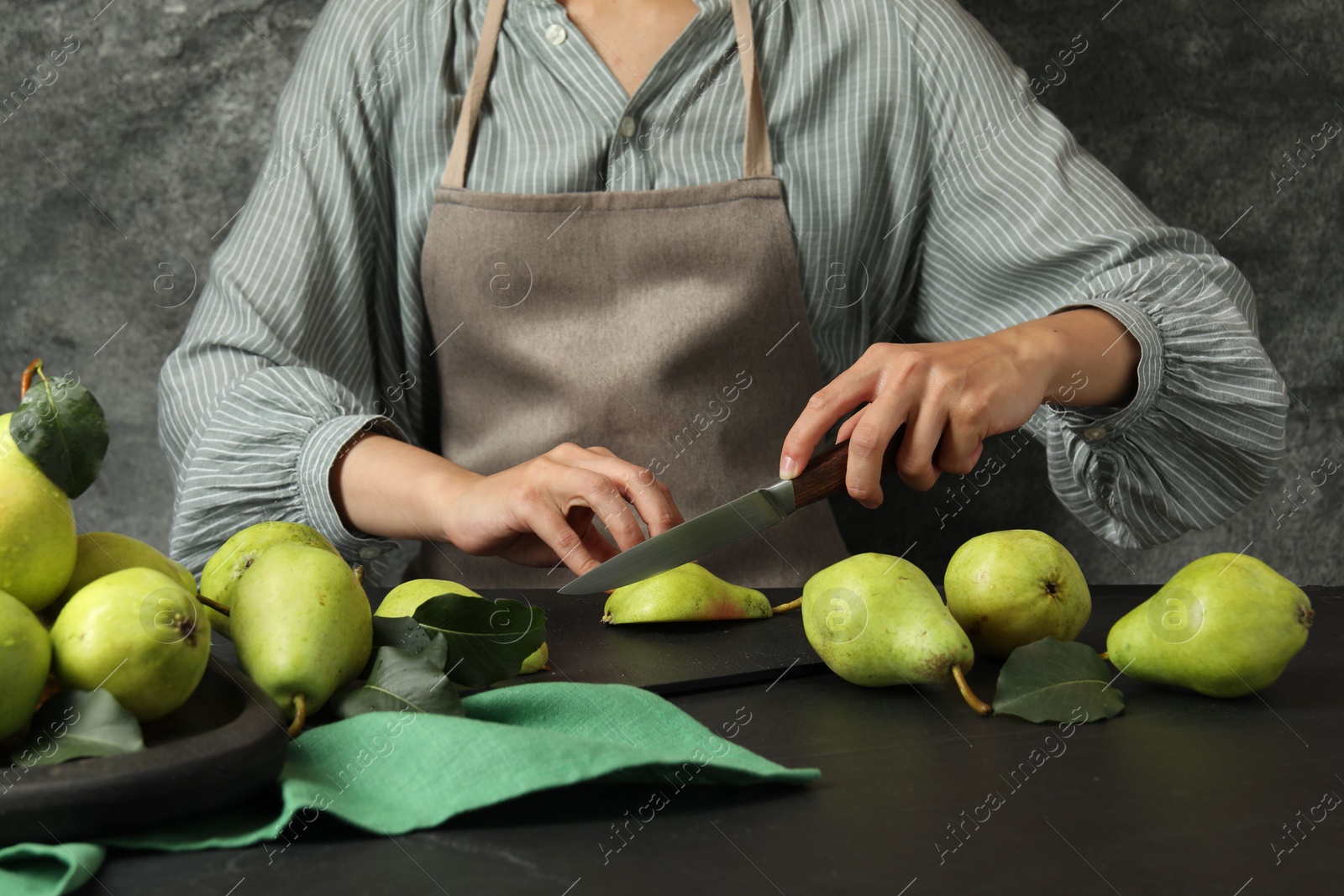 Photo of Woman cutting fresh ripe pear at black table, closeup