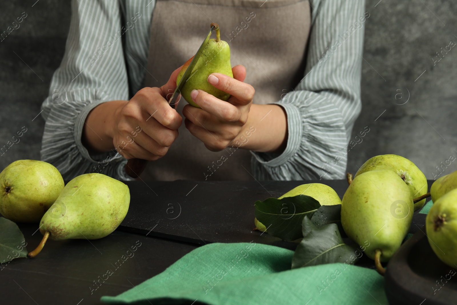 Photo of Woman cutting fresh ripe pear at black table, closeup