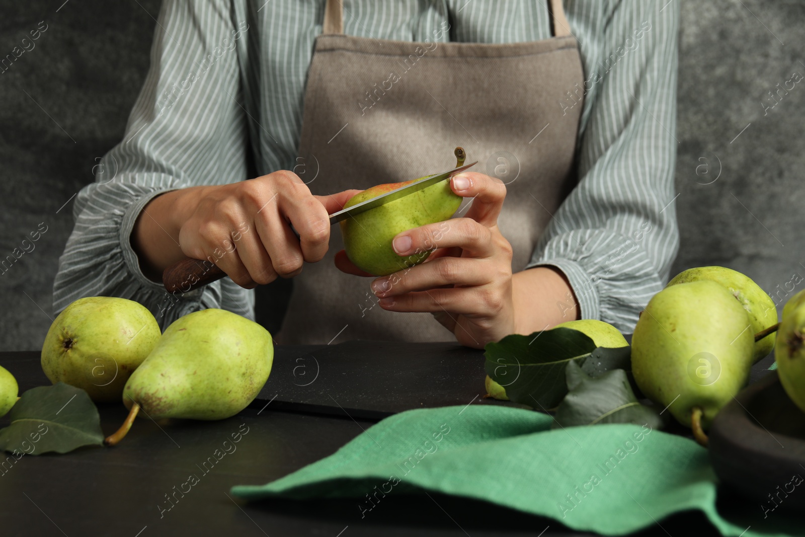 Photo of Woman cutting fresh ripe pear at black table, closeup