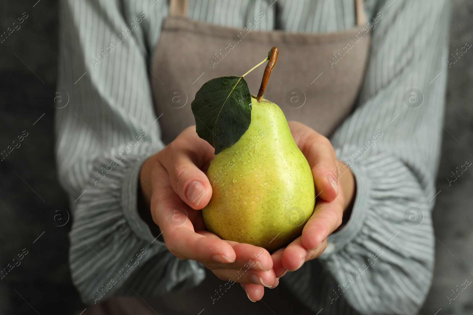 Photo of Woman with ripe pear near grey wall, closeup