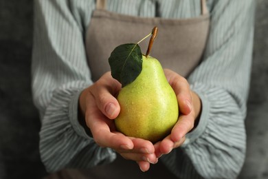 Photo of Woman with ripe pear near grey wall, closeup