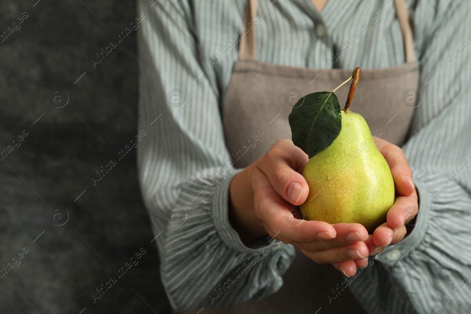 Photo of Woman with ripe pear near grey wall, closeup