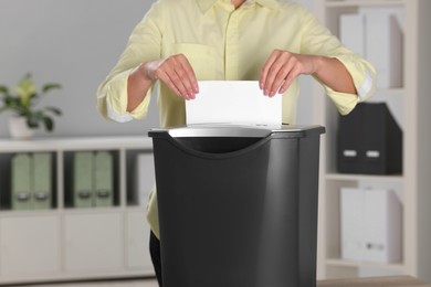 Photo of Woman destroying sheet of paper with shredder in office, closeup