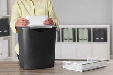 Woman destroying sheet of paper with shredder at wooden table in office, closeup