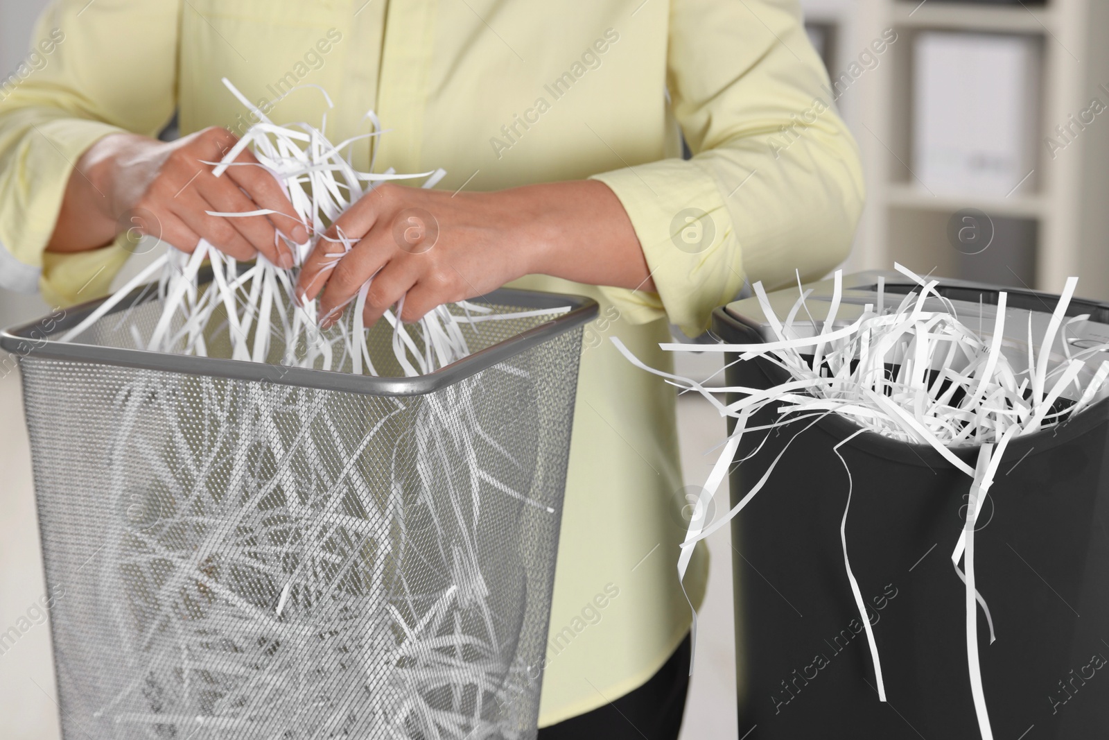 Photo of Woman putting shredded paper strips into trash bin indoors, closeup