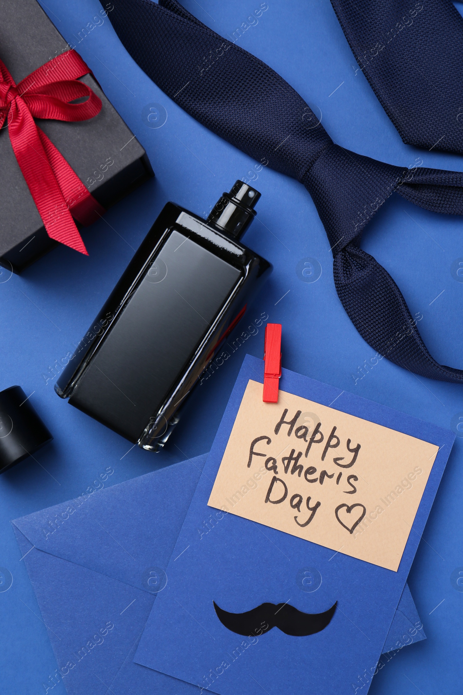 Photo of Greeting card with phrase Happy Father's Day, envelope, bottle of perfume, tie and gift on blue background, flat lay