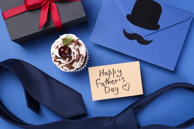 Photo of Greeting card with phrase Happy Father's Day, envelope, tie and gift on blue background, flat lay