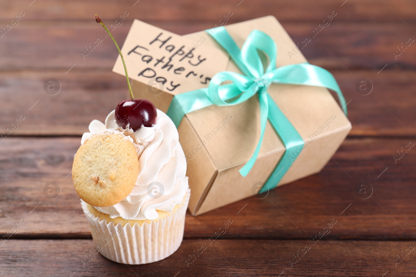 Photo of Happy Father's Day. Cupcake and gift box with card on wooden table, closeup