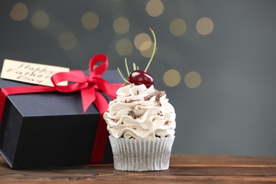 Photo of Happy Father's Day. Cupcake, gift box and card on wooden table against blurred lights, space for text