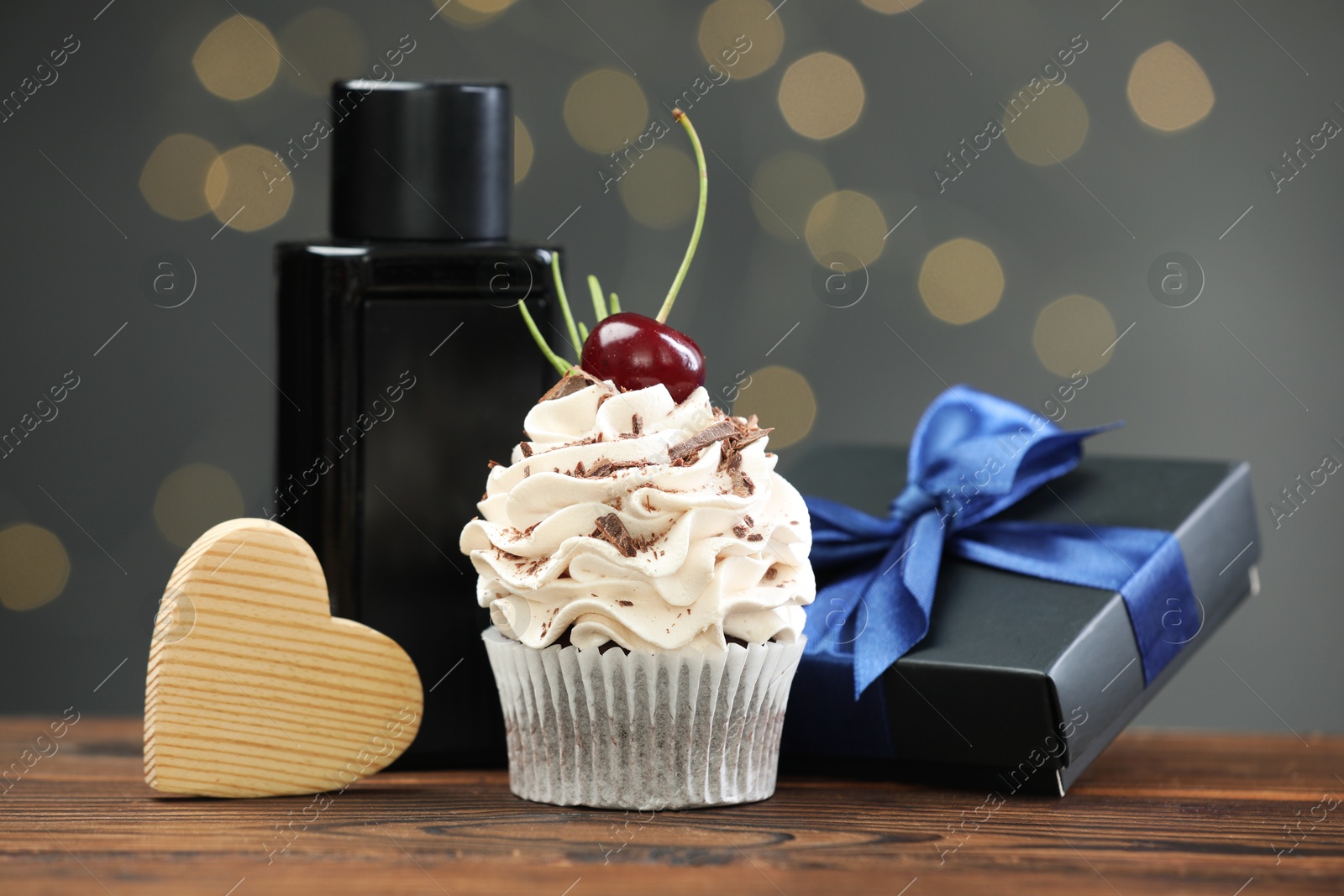 Photo of Happy Father's Day. Cupcake, gift box, wooden heart and perfume on table against blurred lights