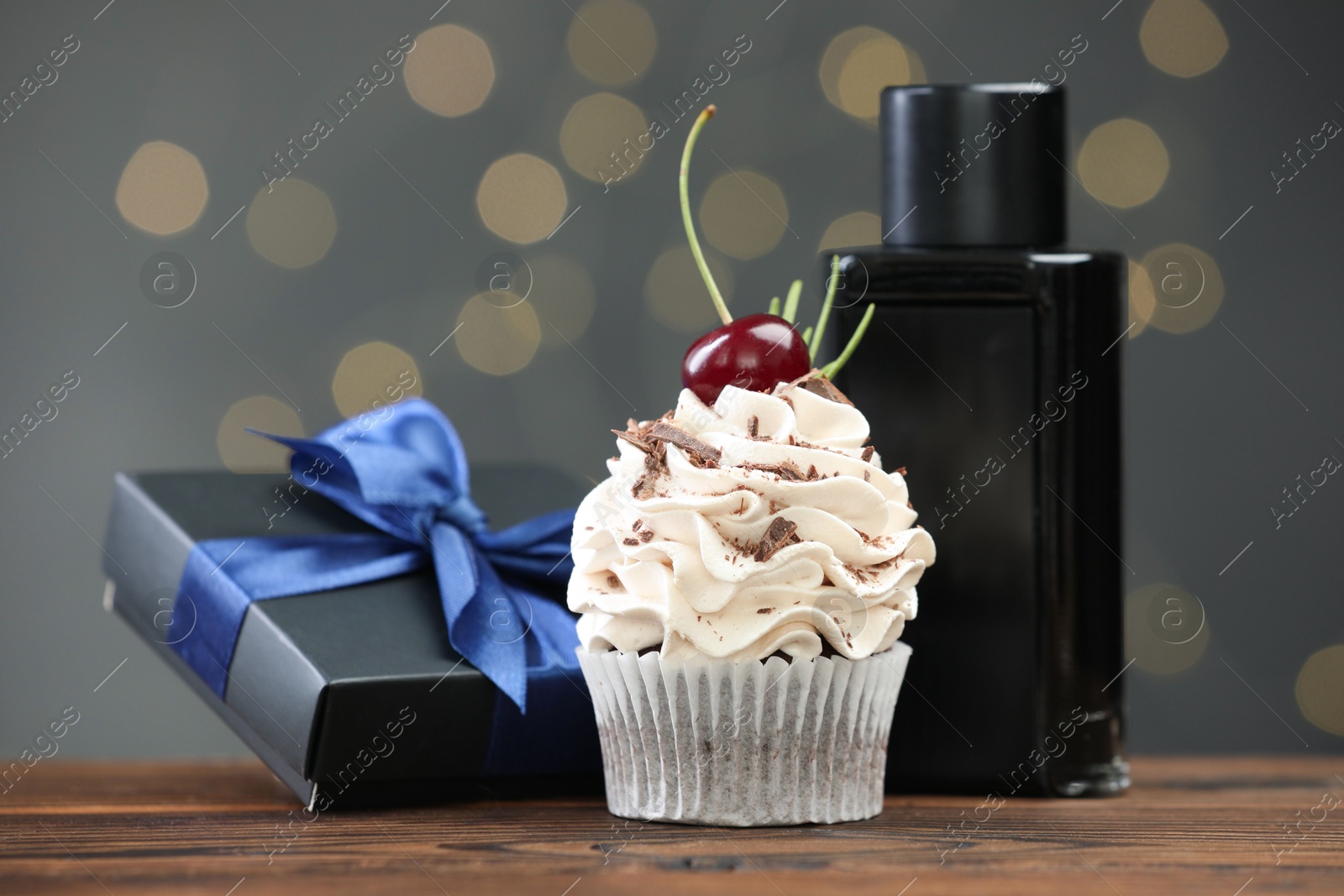 Photo of Happy Father's Day. Cupcake, gift box and perfume on wooden table against blurred lights, closeup