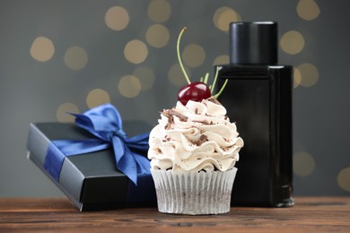 Photo of Happy Father's Day. Cupcake, gift box and perfume on wooden table against blurred lights, closeup