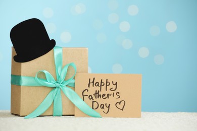 Photo of Greeting card with phrase Happy Father's Day, gift box and paper hat on light table