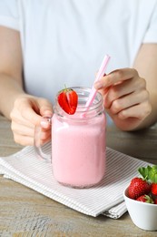 Woman with mason jar of tasty strawberry yogurt at wooden table, closeup