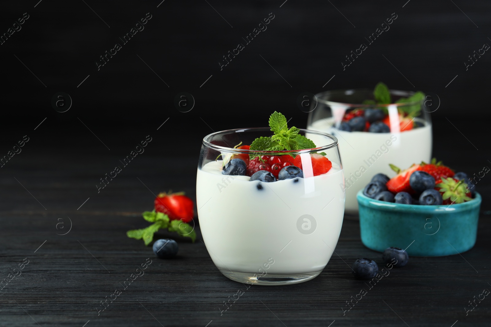 Photo of Tasty yogurt with fresh berries and mint in glasses on black wooden table, closeup. Space for text