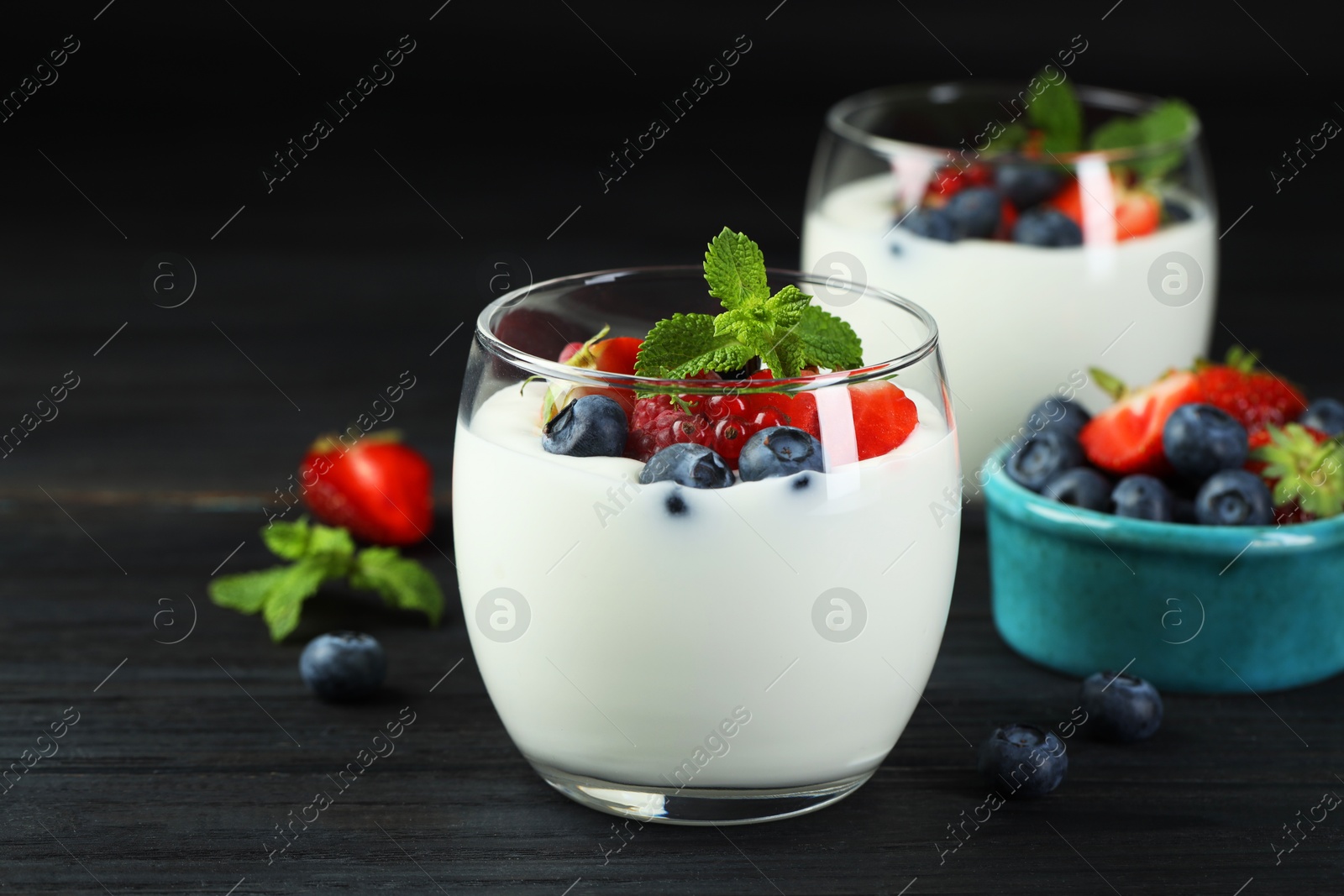 Photo of Tasty yogurt with fresh berries and mint in glasses on black wooden table, closeup