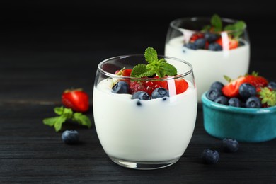 Photo of Tasty yogurt with fresh berries and mint in glasses on black wooden table, closeup